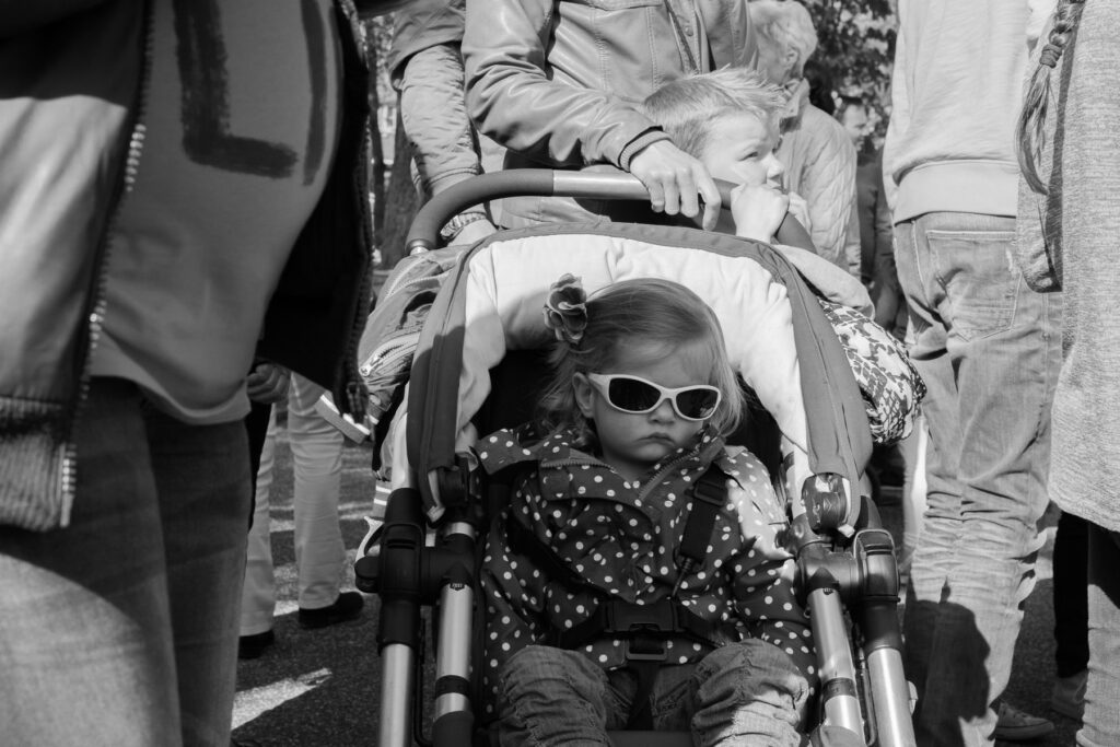 Little girl with big sunglasses resting in her stroller amidst the crowd during the Dutch national holiday Koningsdag (King's Day). 