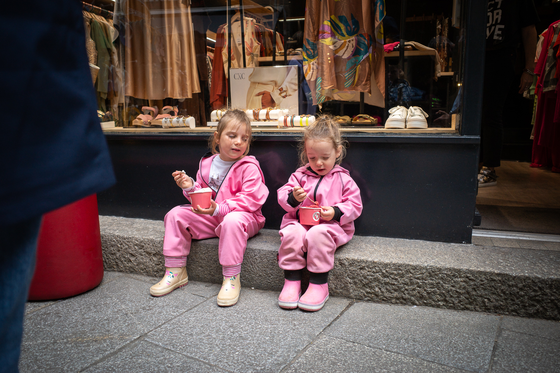 Two little girls dressed in pink overalls eating an ice cream